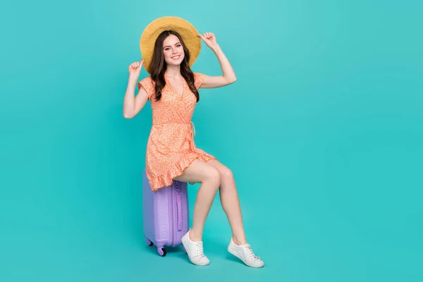 Foto de divertida dama de ensueño vestida de naranja ropa paja sombrero sentado equipaje aislado color verde azulado fondo —  Fotos de Stock