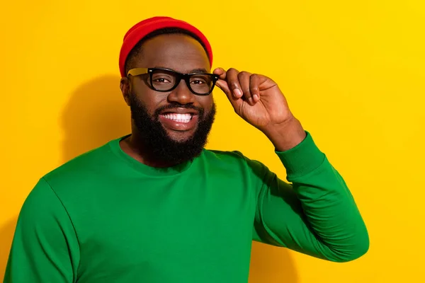 Photo of positive cheerful man toothy smile wear specs red beanie green shirt isolated yellow color background — Zdjęcie stockowe