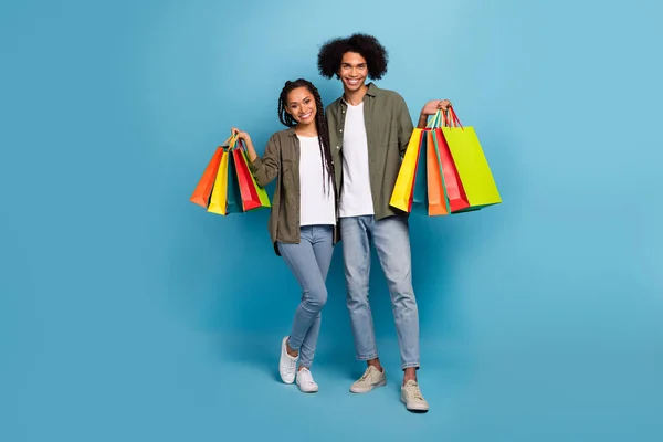 Photo of two friends buyers guy lady hold packages shop center gifts wear shirt denim jeans isolated blue color background — Stockfoto