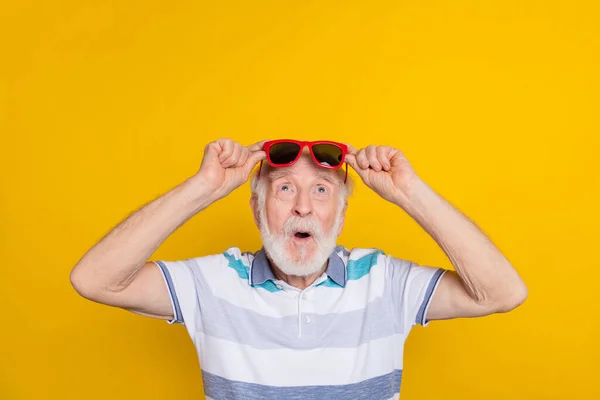 Portrait of attractive amazed grey haired man touching specs wow looking up copy space isolated over bright yellow color background — Photo