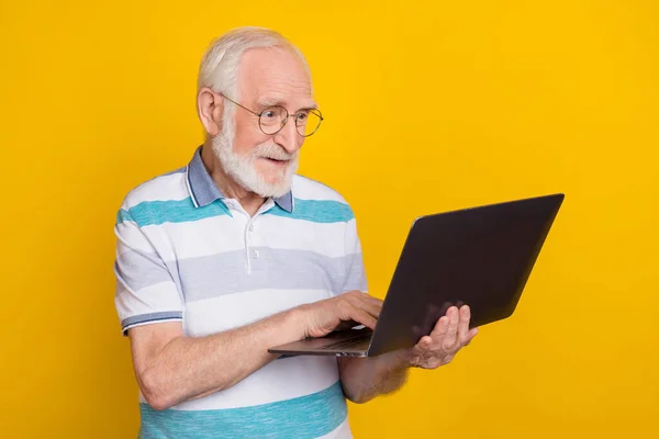 Portrait of attractive cheerful focused grey haired man using laptop writing email isolated over bright yellow color background