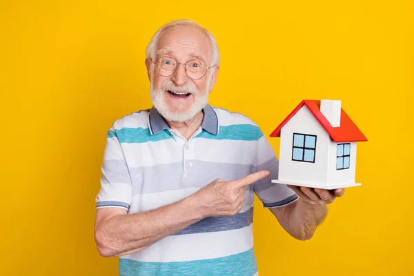 Ritratto di attraente uomo dai capelli grigi allegro dimostrando casa appartamento isolato su sfondo di colore giallo brillante — Foto Stock