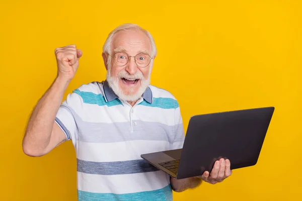 Portrait of attractive amazed cheerful lucky intellectual grey haired man using laptop celebrating isolated over bright yellow color background