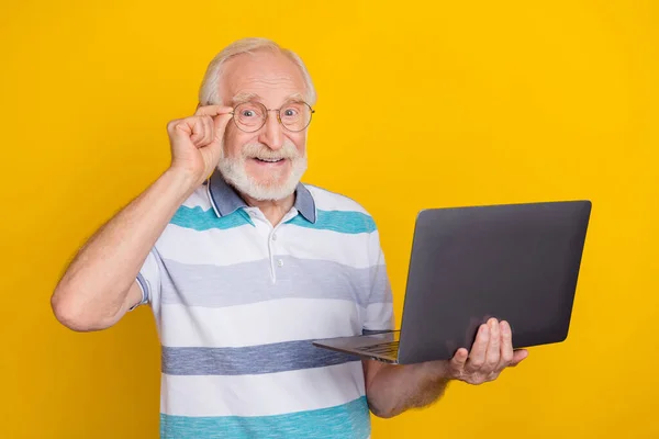 Portrait of attractive cheerful grey haired man using laptop touching specs isolated over bright yellow color background — Fotografia de Stock