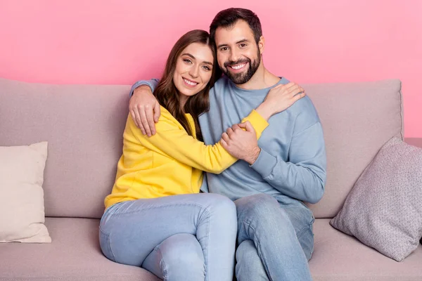 Portrait of attractive cheerful tender couple bonding sitting on divan free time isolated over pink pastel color background — Stockfoto