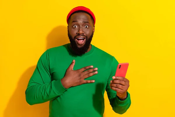 Photo de fou reconnaissant homme tenir téléphone poitrine de palme porter bonnet rouge chemise verte isolé fond de couleur jaune — Photo