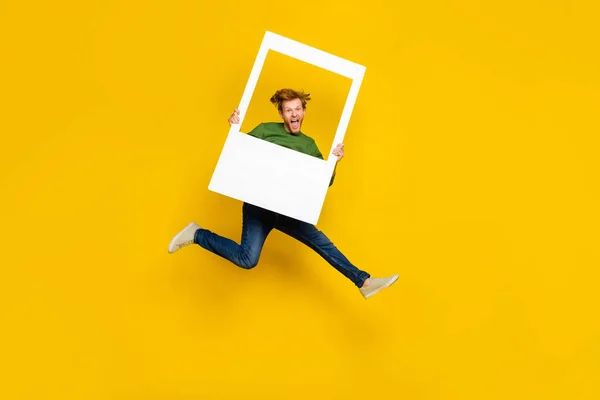 Foto de longitud completa de divertido chico excitado vestido suéter sosteniendo marco de foto blanco aislado color amarillo fondo —  Fotos de Stock