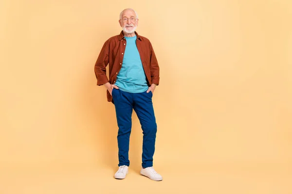 Zdjęcie śmieszne słodkie facet emeryt ubrany brązowy koszula okulary spacery ramiona kieszenie izolowane beżowy kolor tło — Zdjęcie stockowe