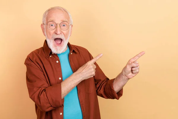Foto de hooray elder gris peinado hombre indican espacio vacío desgaste gafas camisa marrón aislado sobre fondo de color beige —  Fotos de Stock