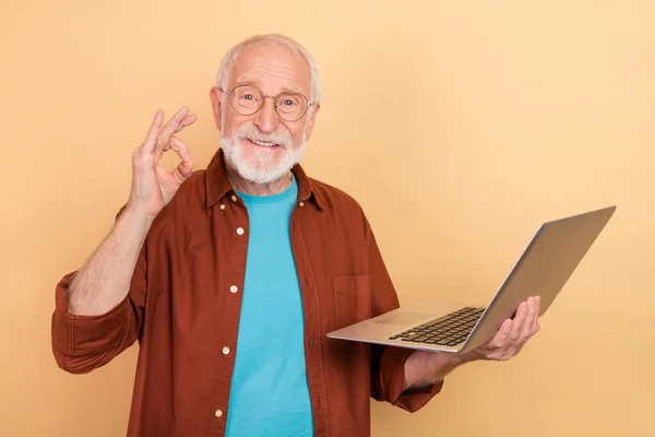 Foto de cara muito engraçado pensioner vestido camisa marrom crescente trabalhando dispositivo moderno okey sinal isolado cor bege fundo — Fotografia de Stock