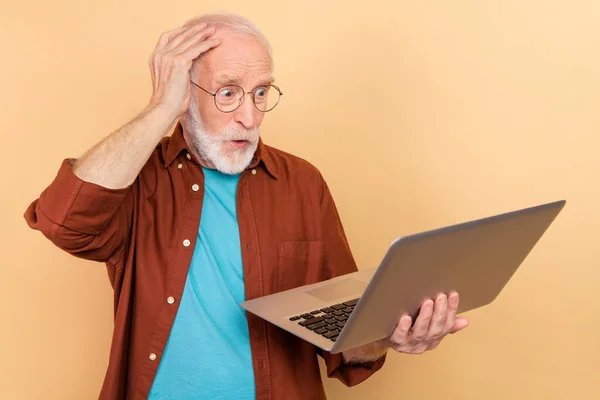 Foto de chocado funky aposentado homem cinza suéter óculos braço cabeça olhando gadget moderno isolado cor bege fundo — Fotografia de Stock