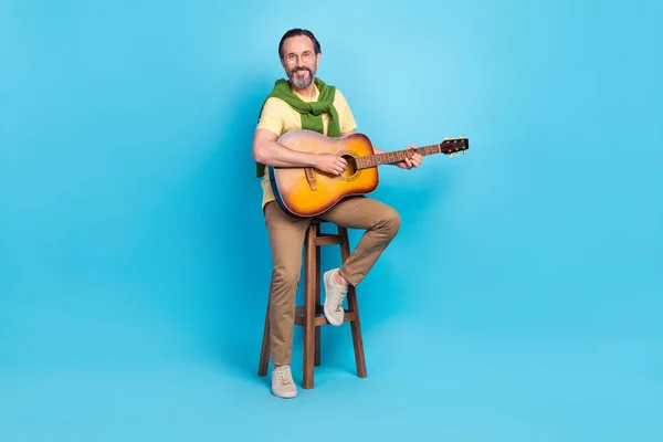 フルサイズの写真明るい青の色の背景に隔離された歌を演奏椅子に座っている陽気な音楽家の — ストック写真
