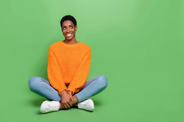 Foto de longitud completa de optimista joven peinado corto señora sentarse look desgaste suéter jeans zapatillas aisladas sobre fondo de color verde —  Fotos de Stock