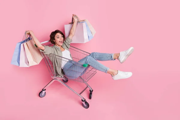 Full size profiel zijkant foto van jonge opgewonden meisje rijden winkelwagentje winkel korting geïsoleerd over roze kleur achtergrond — Stockfoto