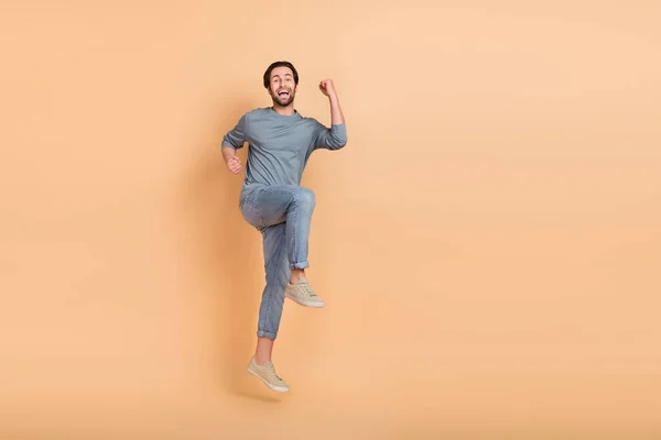 Ganzkörperfoto des jungen aufgeregten Mannes Sprung feiern Glück Triumph Fäuste Hände isoliert über beige Farbe Hintergrund — Stockfoto