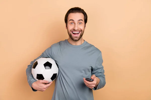 Foto von jungen aufgeregten Kerl hält Ball beobachten Fußballspiel TV-Wochenende isoliert über beige Farbhintergrund — Stockfoto