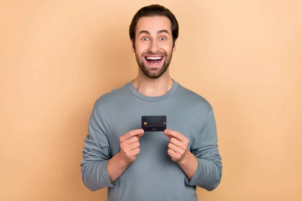 Foto de hombre joven emocionado tarjeta bancaria ahorros ingresos ingresos inversión aislada sobre fondo de color beige — Foto de Stock