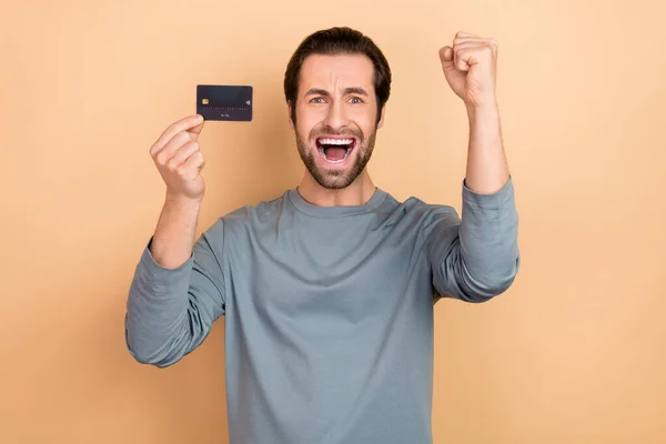 Foto van jonge opgewonden jongen vieren geluk extatische vuisten hand winst besparingen inkomen triomf geïsoleerd over beige kleur achtergrond — Stockfoto