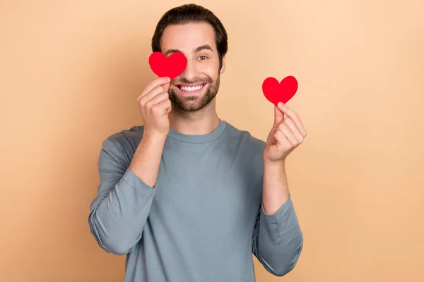 Foto de jovem cara alegre tem divertido tampa olho pouco forma de coração cupido isolado sobre fundo de cor bege — Fotografia de Stock