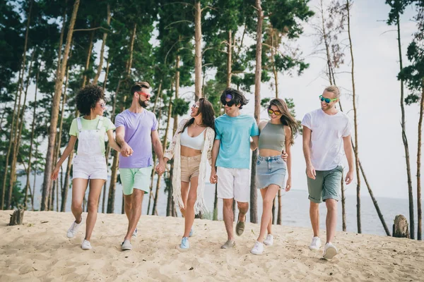 Pleine photo du corps de gais compagnons positifs tiennent bras marchant plage de sable passer du temps libre à l'extérieur — Photo