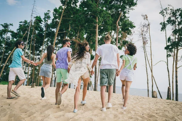 Πλήρες μέγεθος πίσω από τη φωτογραφία των ενθουσιασμένων θετικών ανθρώπων που τρέχουν με τα πόδια παραλία άμμο κρατήστε τα χέρια ζεστό καιρό σε εξωτερικούς χώρους — Φωτογραφία Αρχείου
