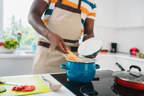 Cropped photo of young guy cooking dish pasta kitchen cuisine saucepan boil eco dieating vermicelli indoors