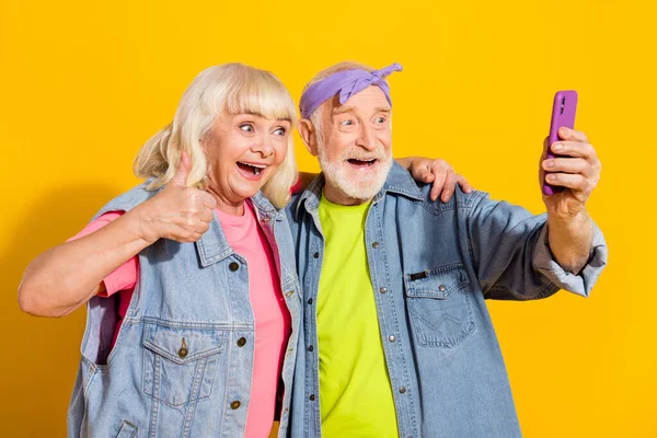 Foto van funky gepensioneerde man vrouw dragen jeans kleding video talk apparaat duim omhoog geïsoleerde gele kleur achtergrond — Stockfoto