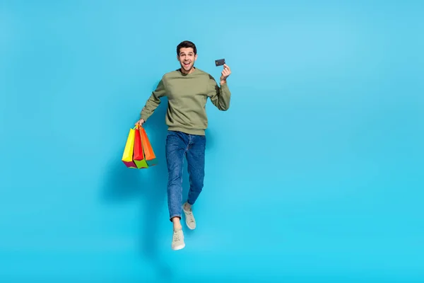 Pełna długość zdjęcie aktywnego energiczny facet trzymać karty debetowej centra handlowe pakiety izolowane na niebieskim tle koloru — Zdjęcie stockowe