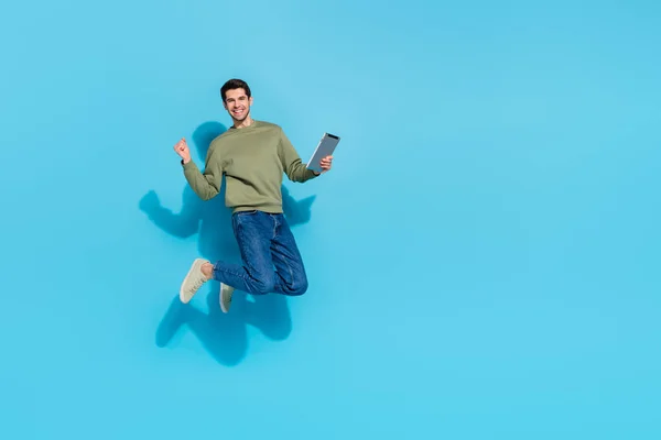 Full length photo of cool millennial brunet guy jump hold tablet φορέστε πουκάμισα τζιν παπούτσια απομονωμένα σε μπλε φόντο — Φωτογραφία Αρχείου