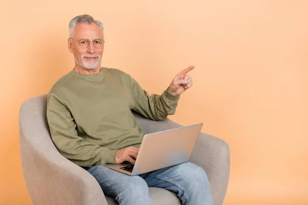 Zdjęcie szefa w wieku siwych włosów człowiek siedzieć z laptopem indeks promo nosić okulary pullover dżinsy izolowane na beżowym tle — Zdjęcie stockowe
