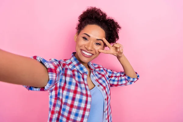 Fotografie sladké vlnité účes dáma do selfie show v-sign oblečení kostkované košile izolované na růžové barevné pozadí — Stock fotografie