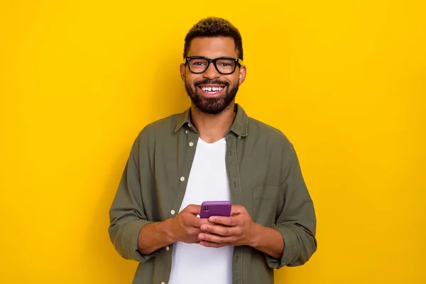 Foto van positieve aantrekkelijke man gekleed groene shirt brillen communiceren moderne gadget geïsoleerde gele kleur achtergrond — Stockfoto