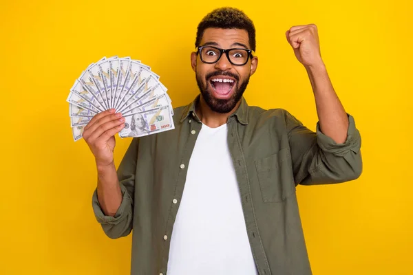 Photo of charming lucky guy dressed green shirt eyewear rising fist money fan isolated yellow color background — Stock Photo, Image