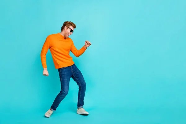 Volledige lengte foto van vrij funky kerel gekleed oranje trui donkere bril dansen lege ruimte geïsoleerde turquoise kleur achtergrond — Stockfoto