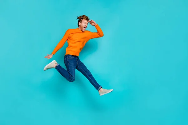 Full length photo of impressed excited guy dressed sweater jumping looking far away empty space isolated turquoise color background — Stock Photo, Image