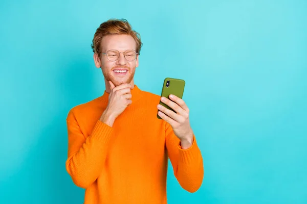 Foto di riflessivo bel giovane uomo indossare arancione pullover occhiali braccia mento lettura dispositivo moderno isolato colore verde acqua sfondo — Foto Stock
