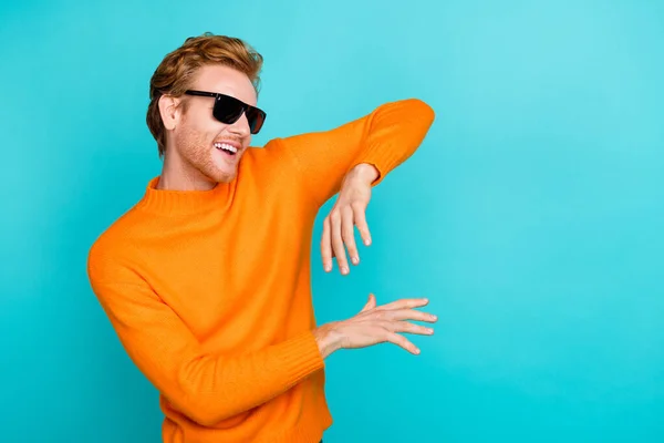 Foto van koele mooie jongen gekleed oranje trui donkere bril dansen lege ruimte geïsoleerde turquoise kleur achtergrond — Stockfoto