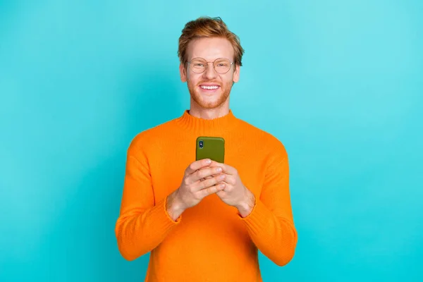 Foto di dolce affascinante ragazzo vestito arancione maglione occhiali digitando dispositivo moderno isolato colore turchese sfondo — Foto Stock
