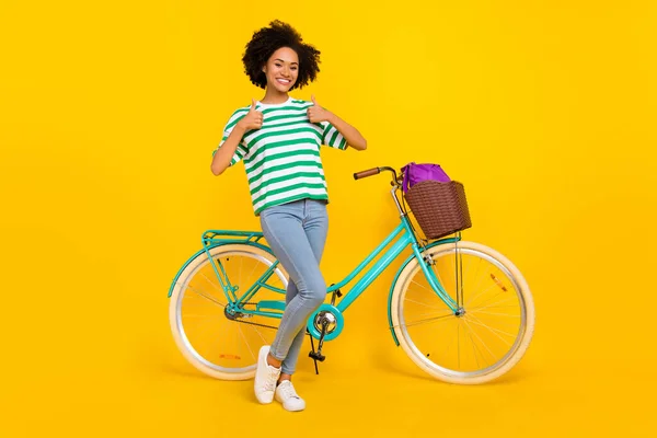 Foto de comprimento total de funky jovem senhora perto de bicicleta polegar até desgaste t-shirt jeans sapatilhas saco isolado no fundo amarelo — Fotografia de Stock