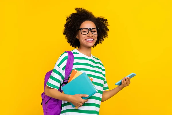 Foto di bella signora millenaria bruna tenere telefono libro usura occhiali t-shirt borsa isolato su sfondo giallo — Foto Stock