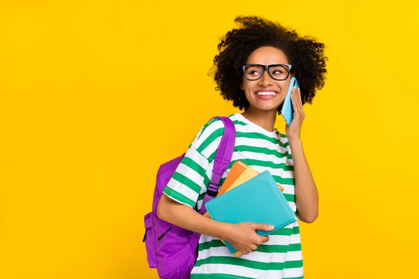 Foto de engraçado jovem morena senhora dizer telefone segurar livro olhar promo usar óculos t-shirt saco isolado no fundo amarelo — Fotografia de Stock