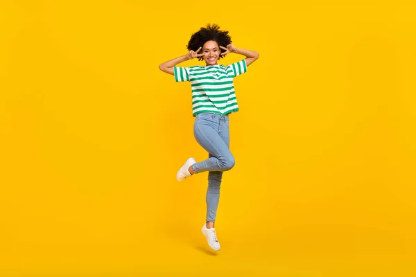 Foto de cuerpo completo de cool millennial lady jump show v-sign wear camiseta jeans zapatillas aisladas sobre fondo amarillo — Foto de Stock