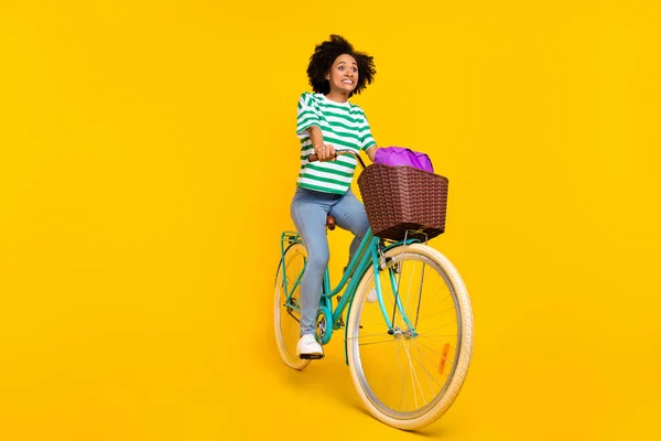 스트레스를 받는 밀레니엄 여성 자전거타는 모습의 전신 사진은 노란 배경에 고립된 티셔츠 청바지 신발 가방을 착용하고 있다. — 스톡 사진
