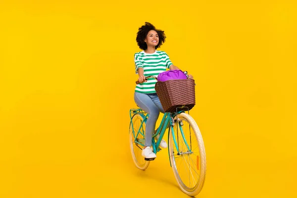 Foto em tamanho completo de funky jovem senhora passeio de bicicleta olhar para cima desgaste t-shirt jeans sapatos saco isolado no fundo amarelo — Fotografia de Stock