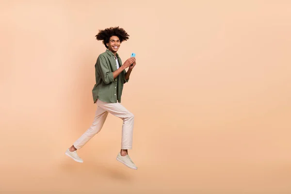 Perfil de tamaño completo retrato de guapo chico alegre mantener el teléfono divertirse aislado sobre fondo de color beige — Foto de Stock