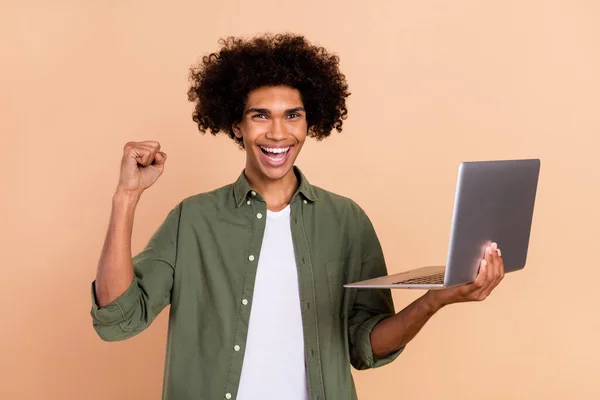 Portrét atraktivní veselý šťastný vlnité-vlasy chlap pomocí notebooku radovat se baví izolované přes béžové pastelové barvy pozadí — Stock fotografie