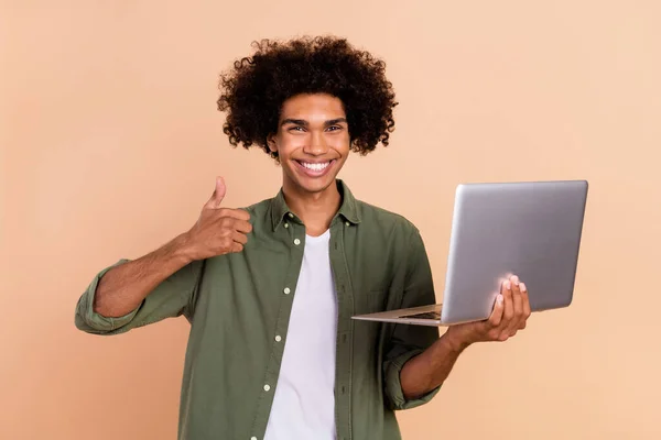 Retrato de guapo de moda alegre tipo de pelo ondulado utilizando el ordenador portátil que muestra pulgar aislado sobre fondo de color pastel beige —  Fotos de Stock