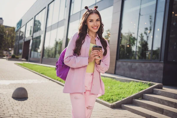 Retrato de atraente alegre menina de cabelos ondulados bebendo bebida indo para a faculdade passar o dia ao ar livre — Fotografia de Stock