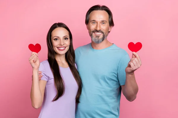 Ritratto di partner positivi tenere mostrano piccolo simbolo del cuore di carta rossa isolato su sfondo di colore rosa — Foto Stock