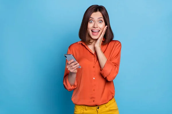 Портрет привлекательной веселой удивленной девушки с помощью устройства блоггинга весело изолированы на ярко-голубом фоне — стоковое фото